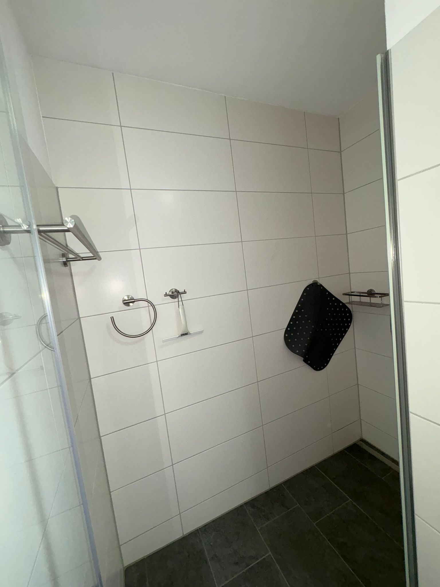 A bathroom with white tiled walls, a shower area, and a dark tiled floor.