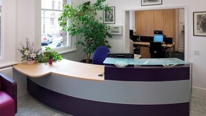 A reception desk with a curved design, a large potted plant, and a view of the street outside. - Student Only Old Kent Road (London)