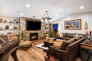 A living room with a stone fireplace, leather sofa, wooden coffee table, and a television mounted on the wall. - Amazing Reviews - 10 Beds, 5 Br, Saloon,Jail,Spa! (Temecula)