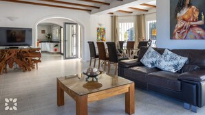 A modern living room with a glass coffee table, leather sofa, and dining area with chairs. - Villa AVETA by Abahana Villas (Moraira)