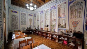 A dining area with ornate tile work, wooden furniture, and a long counter with dishes and glasses. - Kavsar Hotel (Bukhara)