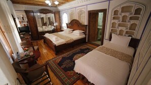 A traditional room with a large bed, a wooden desk, and a mirror. - Kavsar Hotel (Bukhara)
