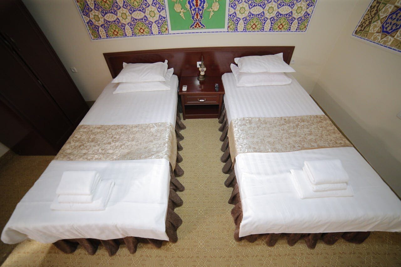 A double room with two beds, a nightstand, and a decorative wall panel.