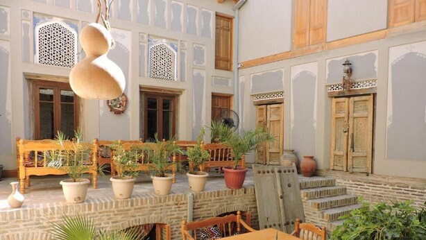 A courtyard with wooden furniture, potted plants, and traditional doors. - Kavsar Hotel (Bukhara)