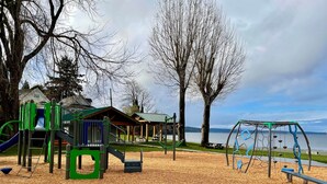 A playground with a slide, swings, and a covered seating area near a body of water.