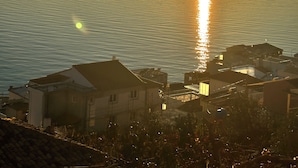 A coastal view with a sunset over the sea, buildings in the foreground, and a clear sky.