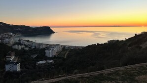 A coastal town with buildings along the shoreline, a clear sky, and a sunset over the water.