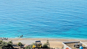 A coastal view with a clear sky, calm sea, and a sandy beach with some structures.