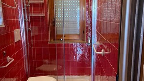 A bathroom with red tiled walls, a shower enclosure, a toilet, and a sink. - Apartment with access to the Costa dei Trabocchi bike path (ortona)