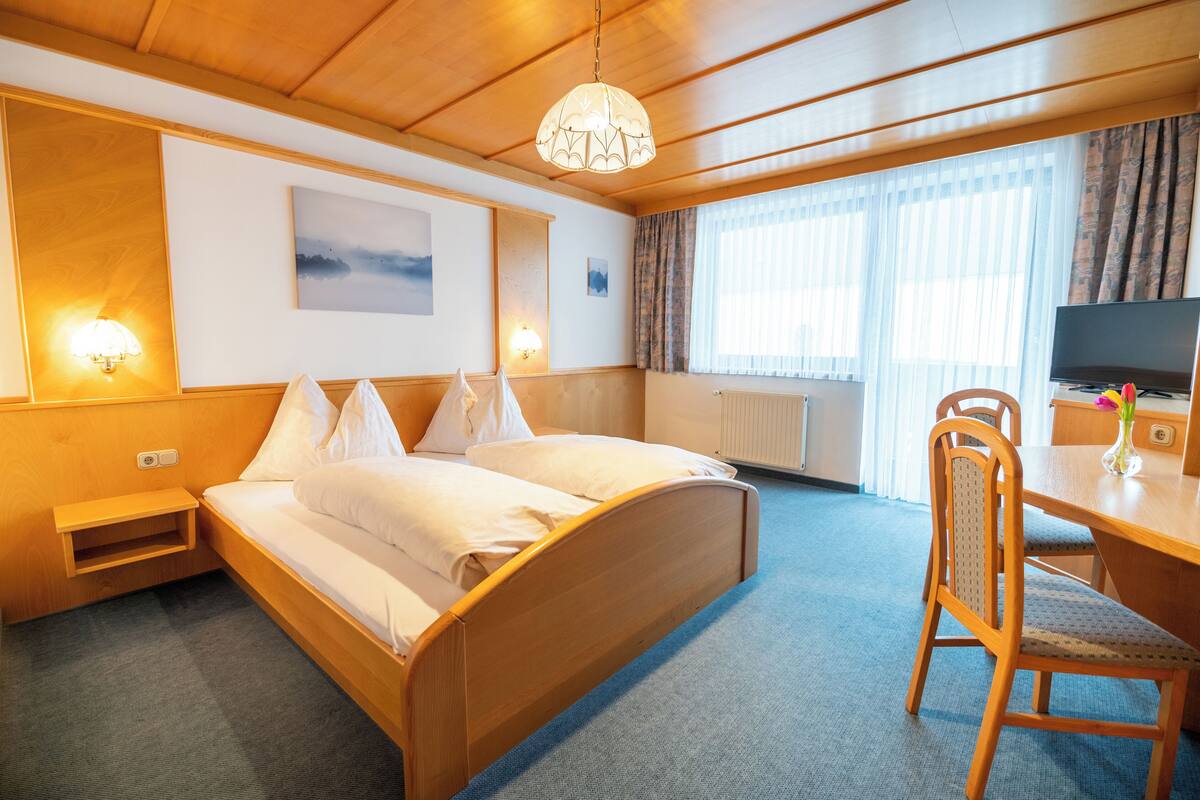 A hotel room with a wooden bed, a desk with a chair, a television, and a window with curtains.