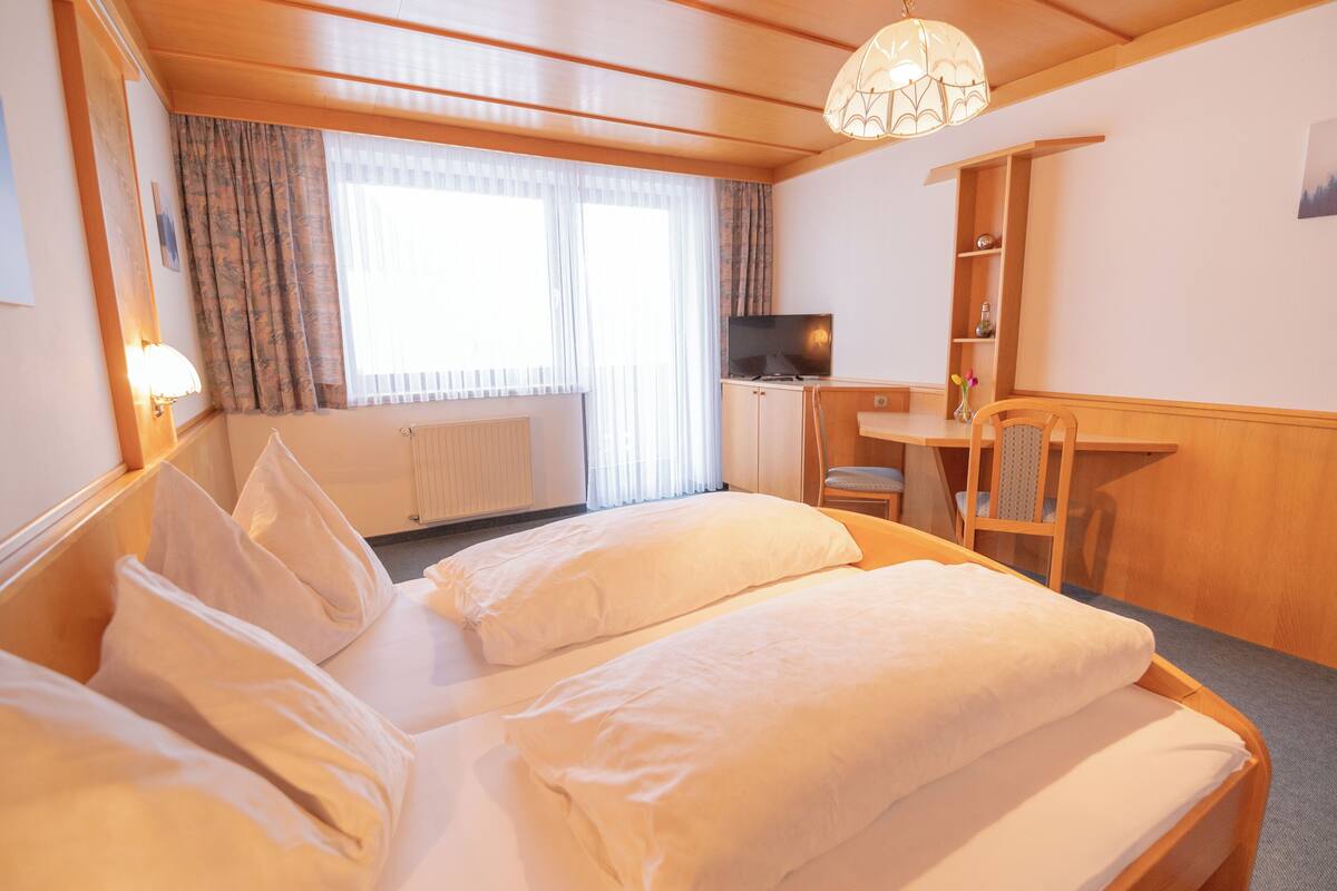 A hotel room with a bed, a desk, a chair, a television, and a window with curtains.