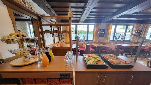 A buffet setup with various food items and beverages, a seating area with red cushioned chairs, and a view of the outdoors through large windows. - Kirchenwirt St. Aegidi (St. Aegidi)