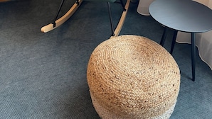 A teal upholstered rocking chair with wooden legs, a woven round ottoman, and a small round table with a black frame. - Kirchenwirt St. Aegidi (St. Aegidi)