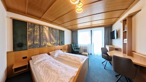 A hotel room with two beds, a desk, a chair, a TV, and a large forest mural on the wall. - Kirchenwirt St. Aegidi (St. Aegidi)