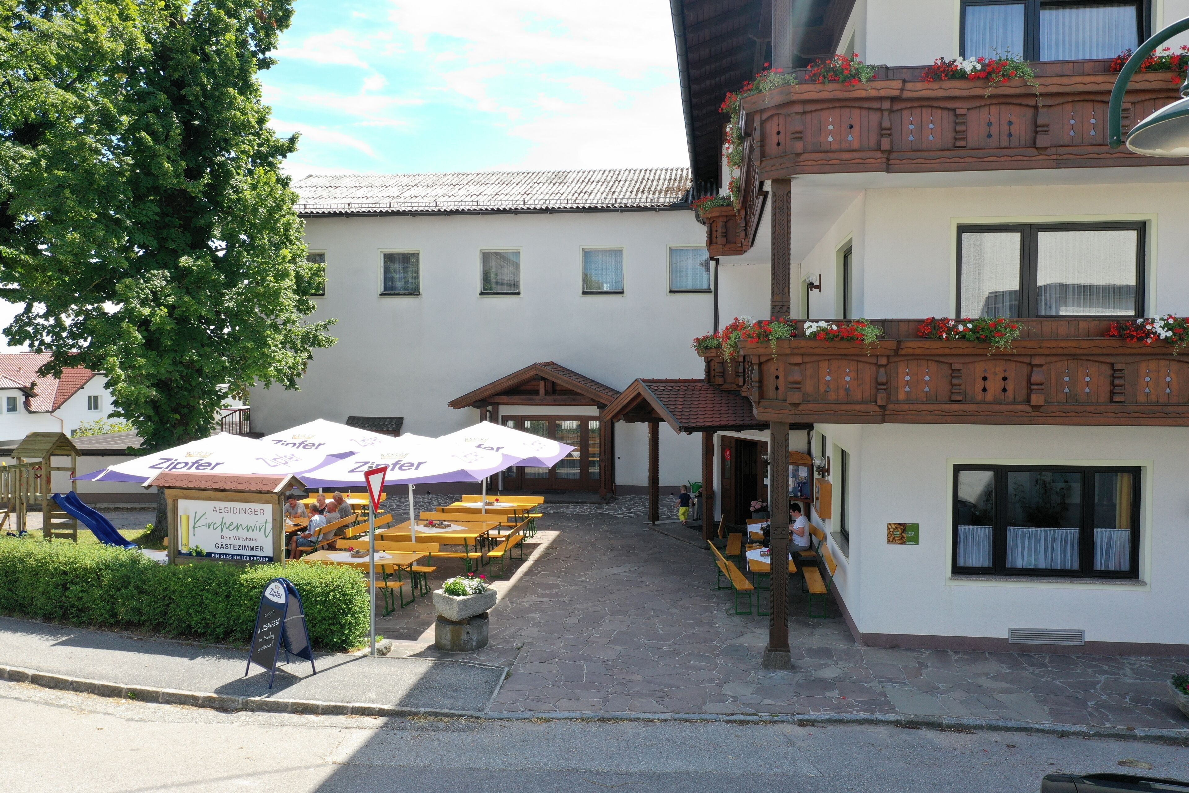 A building with outdoor seating, a sign for a restaurant, and a wooden balcony with flowers.