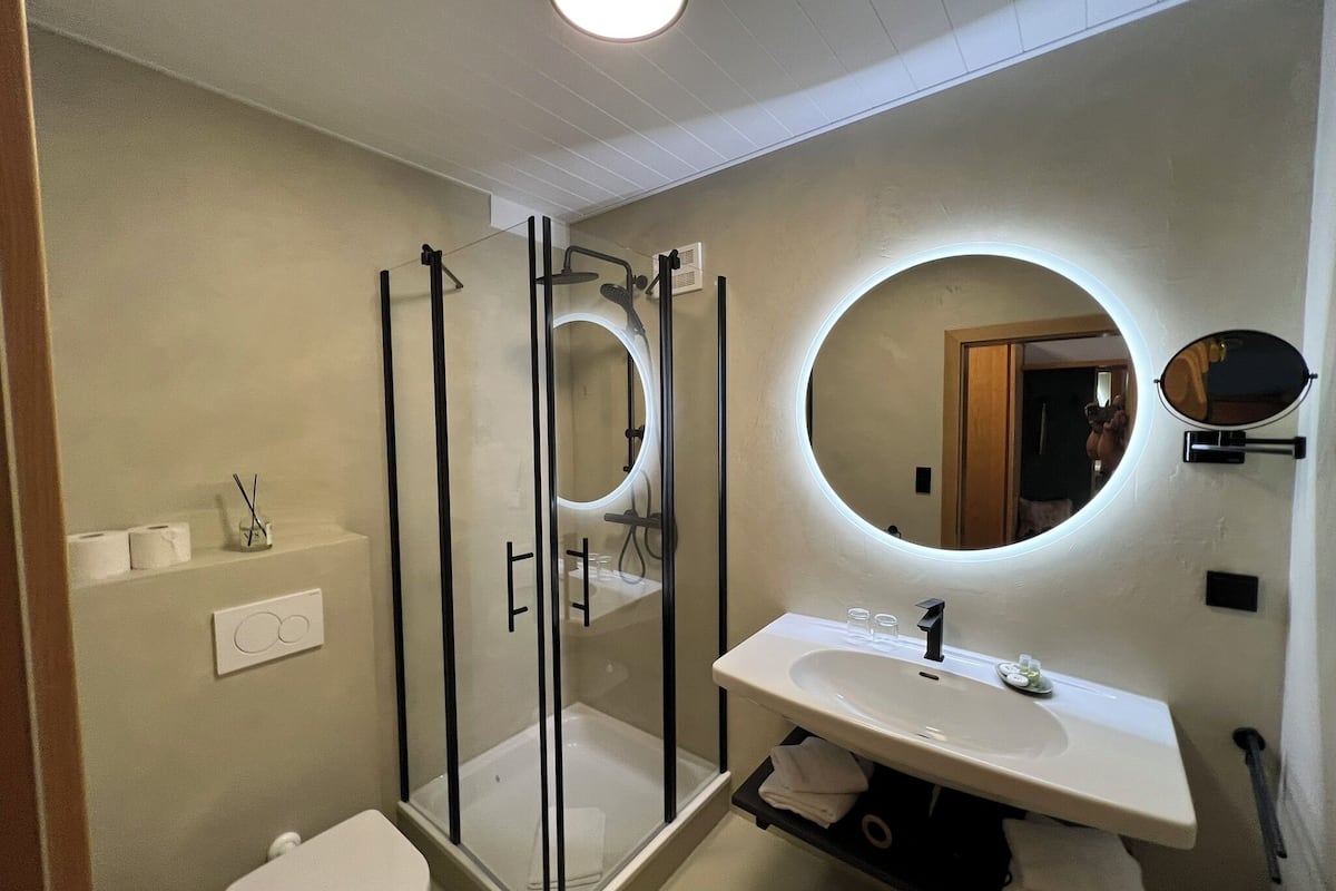 A modern bathroom with a glass-enclosed shower, a round mirror above the sink, and a toilet.