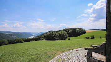 A cobblestone path leading to a wooden bench overlooking a green field and forested hills.