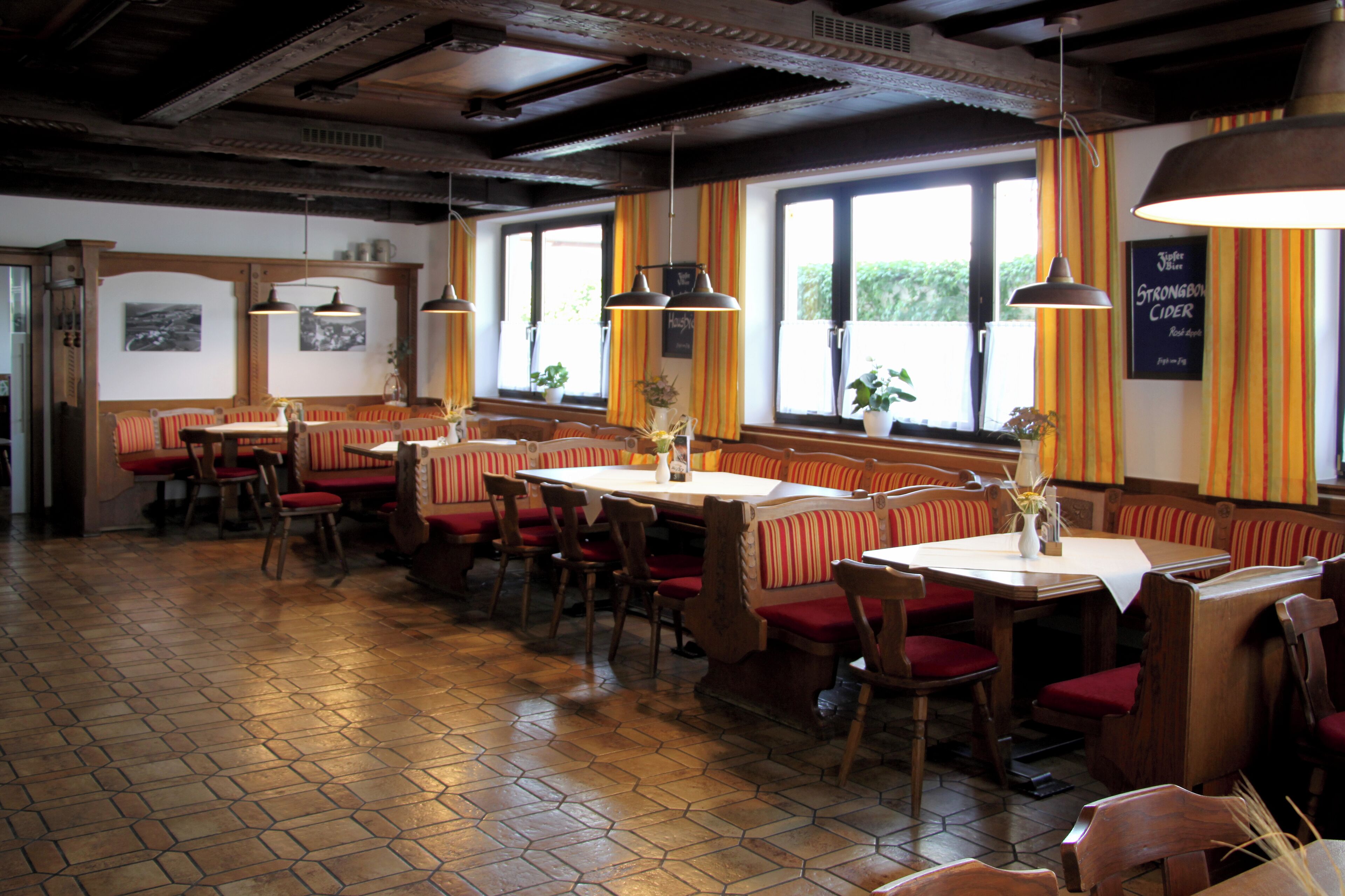 A restaurant with wooden booths and tables, large windows with curtains, and hanging pendant lights.