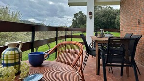 Un patio al aire libre con una mesa y sillas, una silla de mimbre y vistas a un paisaje verde.
