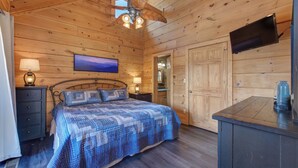 A wooden cabin bedroom with a bed, nightstands, a ceiling fan, a TV, and a wooden door. - Spacious 4BD Cabin w/ Hot Tub! Fireplaces + GAMES! (Sevierville)