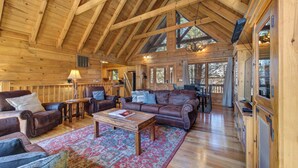A spacious wooden interior with a high ceiling, leather furniture, and large windows. - Spacious 4BD Cabin w/ Hot Tub! Fireplaces + GAMES! (Sevierville)