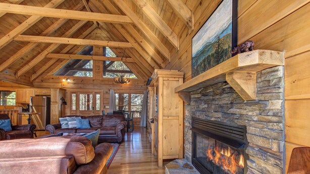 A spacious living room with a stone fireplace, wooden beams, and leather furniture. - Spacious 4BD Cabin w/ Hot Tub! Fireplaces + GAMES! (Sevierville)