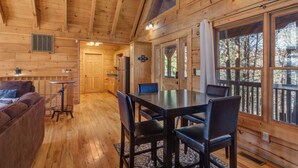 A wooden cabin interior with a dining area, a sofa, and large windows. - Spacious 4BD Cabin w/ Hot Tub! Fireplaces + GAMES! (Sevierville)