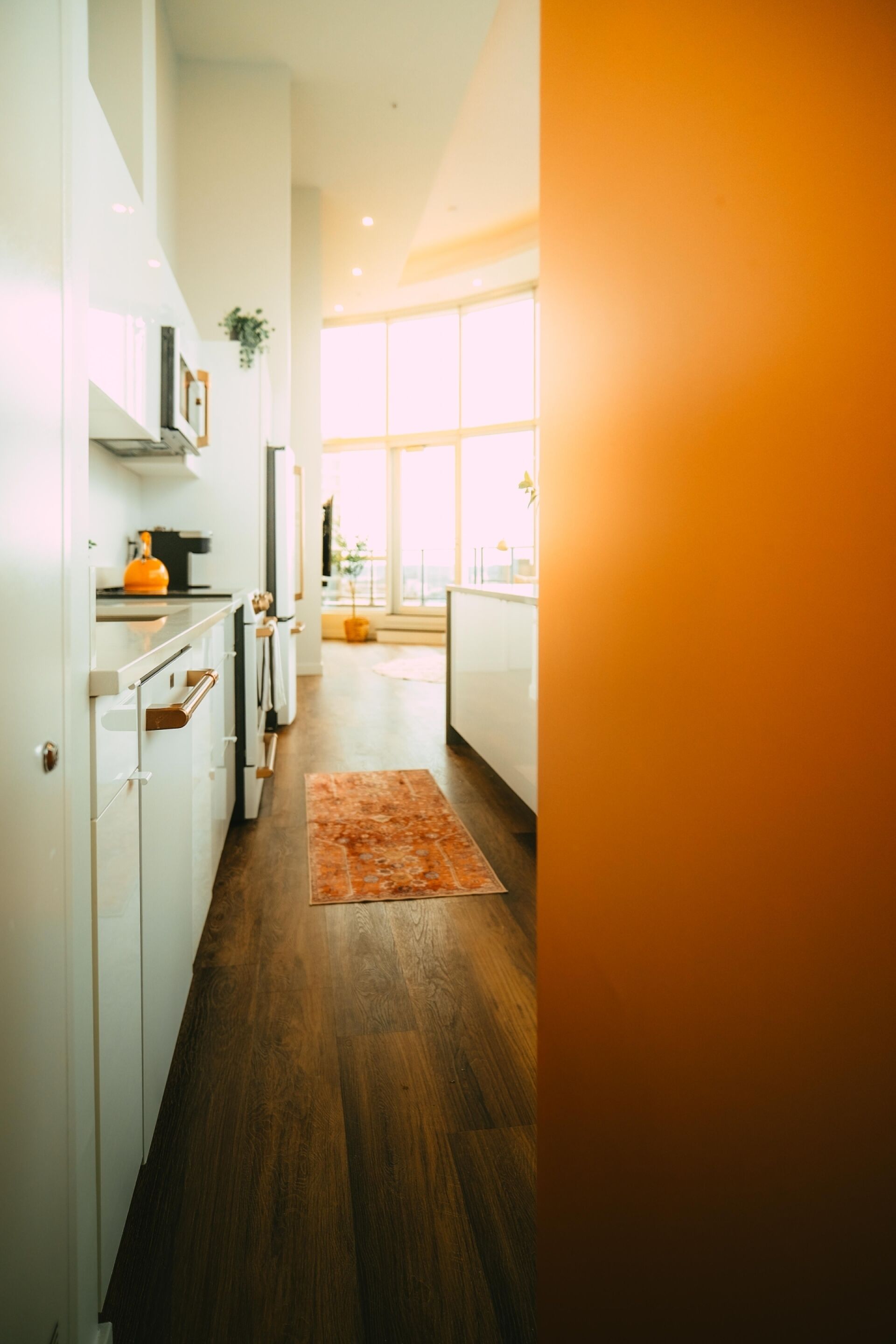 A modern kitchen with white cabinets, a wooden floor, and a large window providing natural light.