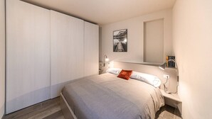 Um quarto com uma cama, mesa de cabeceira, luminária, prateleira na parede e guarda-roupa.