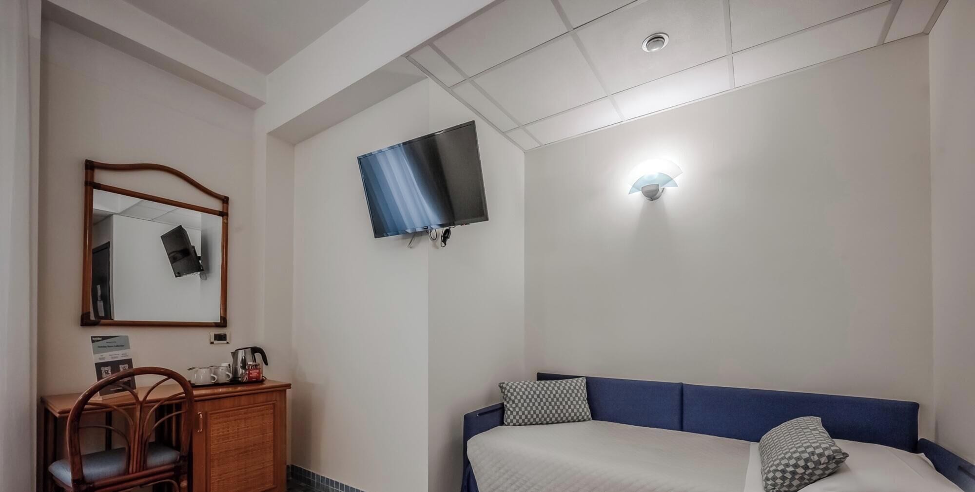 A bedroom with a bed, a dresser, a mirror, and a television mounted on the wall.
