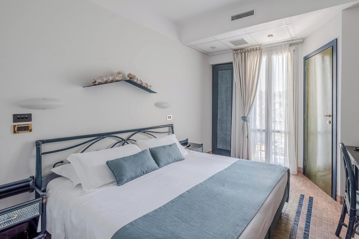 A hotel room with a bed, a desk, and a view of the outside.