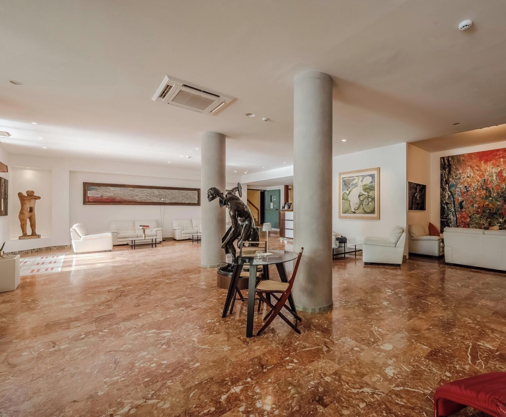 Een ruime lobby met marmeren vloer, witte banken, een sculptuur en kunstwerken aan de wanden.