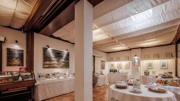 Comedor de hotel con mesas dispuestas para el desayuno, obras de arte en las paredes y una barra de buffet.