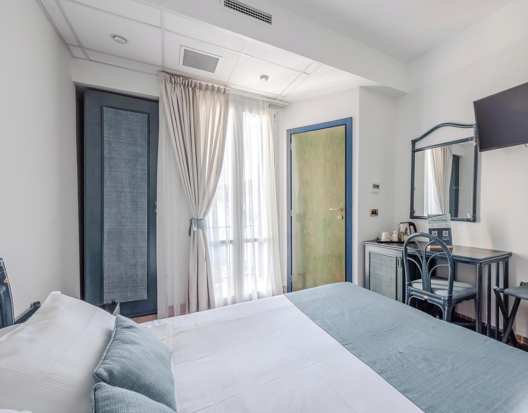 Une chambre d’hôtel avec un lit, un bureau, une chaise, un miroir et une porte.