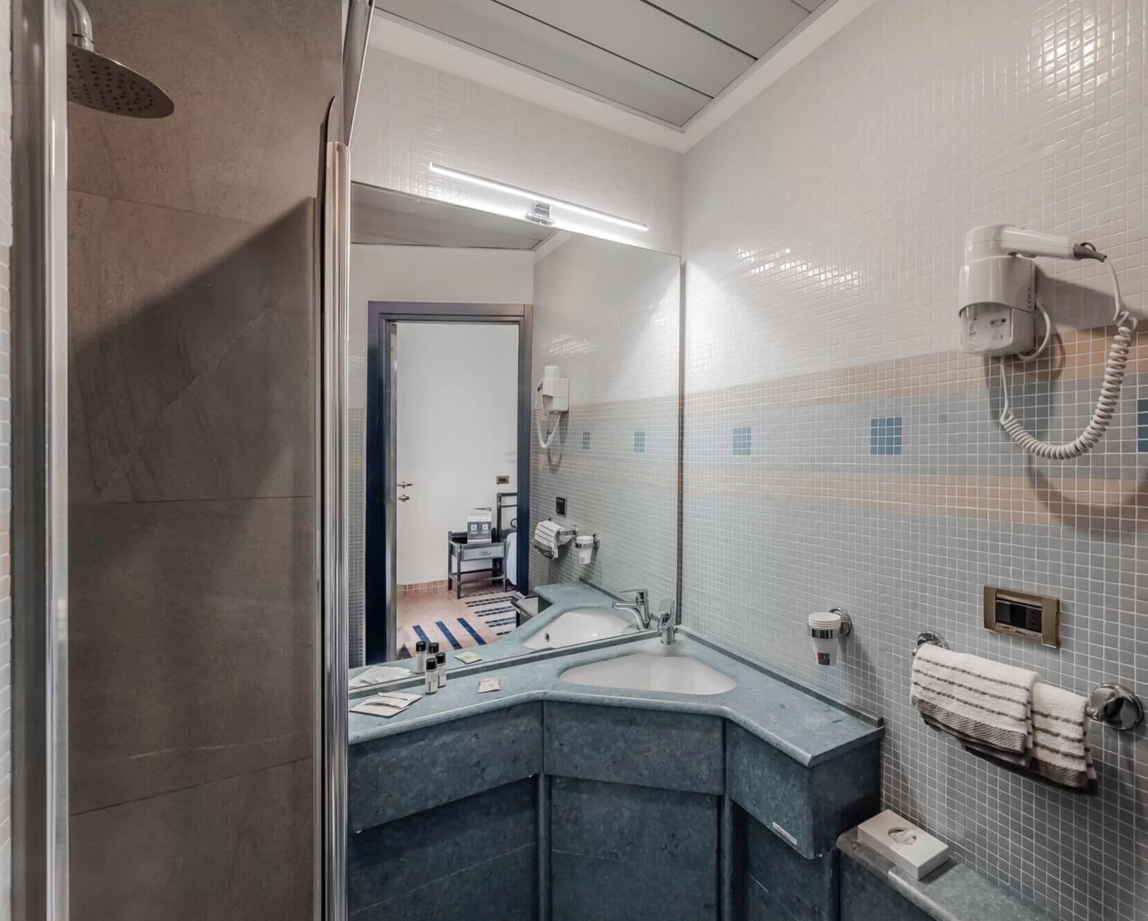 A modern bathroom with a large mirror, a shower, a sink, and a towel rack.