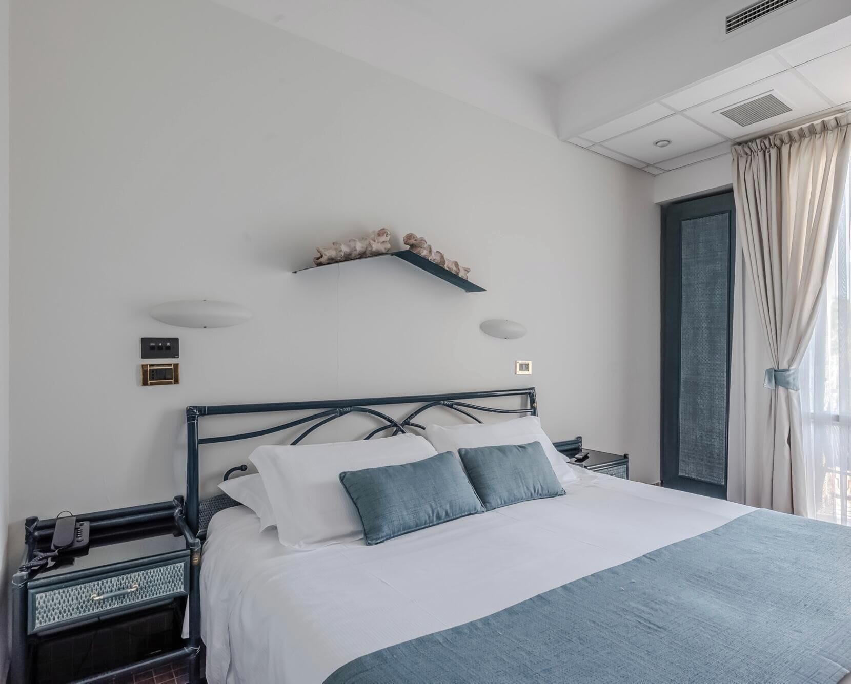 A neatly made bed with a headboard, bedside tables, and a wall-mounted shelf above it.