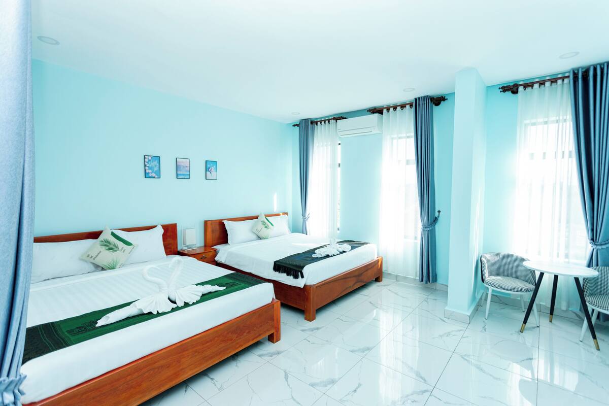 A hotel room with two wooden beds, a small round table, and a chair.