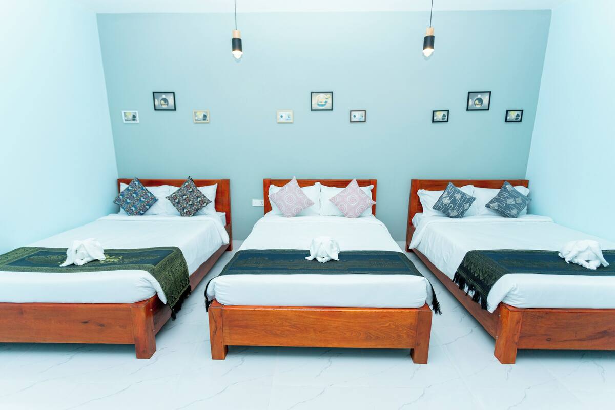 A hotel room with three wooden beds, each with a white mattress and patterned pillows.