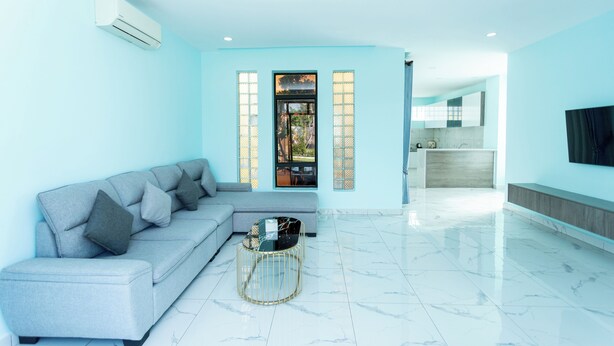 A modern living room with a grey sofa, a round coffee table, and a kitchen area in the background. - LML Kampot Relax House (Kampot)