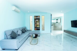 A modern living room with a grey sofa, a round coffee table, and a kitchen area in the background.