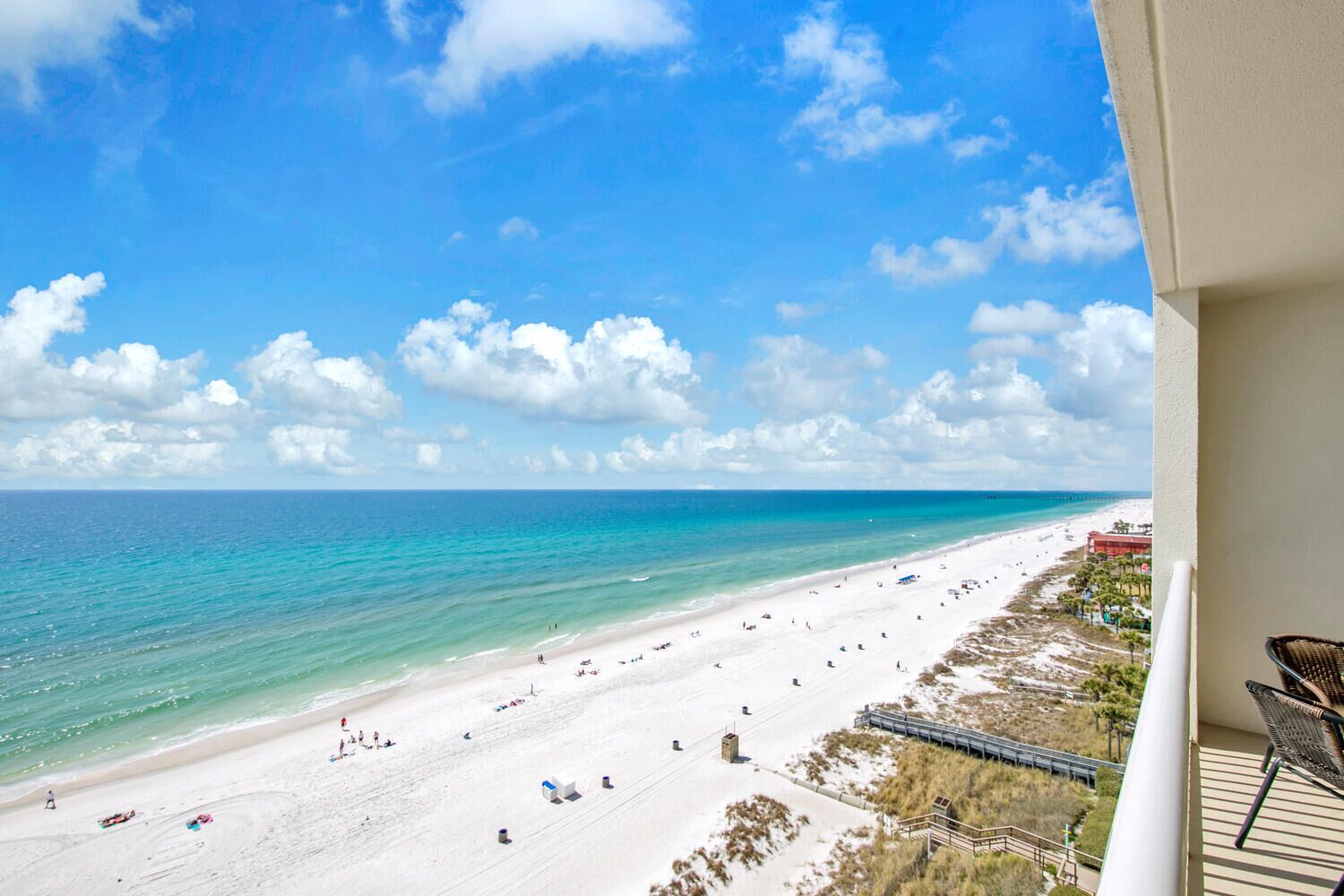 Blick auf einen Strand vom Balkon aus, mit blauem Himmel, Sandstrand und einigen Personen.
