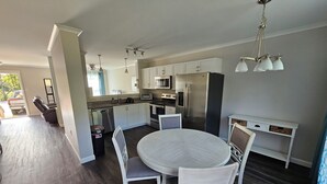 Una cocina moderna con armarios blancos, un refrigerador de acero inoxidable y un comedor con una mesa redonda y sillas blancas.