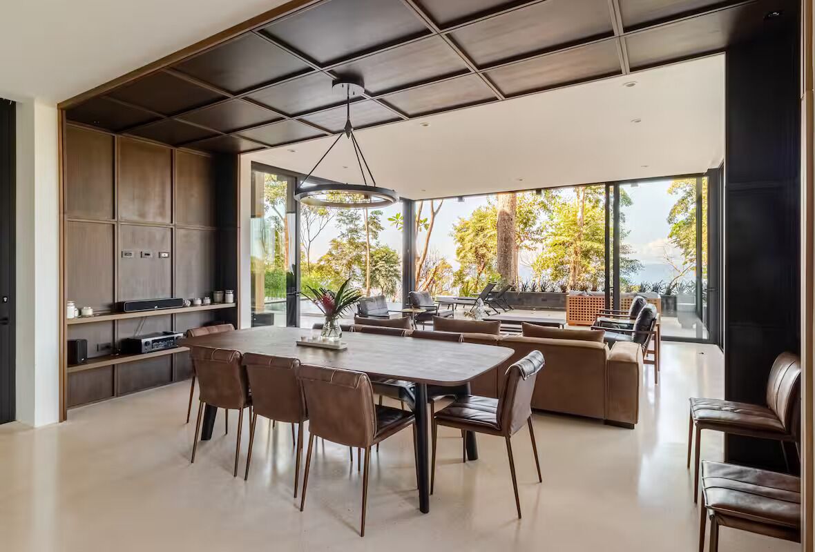 A modern kitchen with a dining area, large windows, and a view of the outdoors.