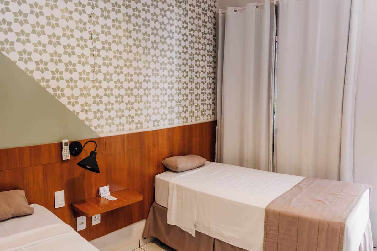 Habitación de hotel con dos camas, cabecero de madera, pared con diseño, lámpara de noche y cortina.