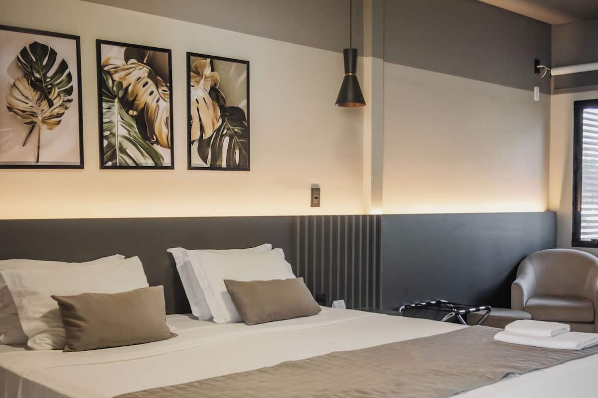 Una habitación de hotel moderna con una cama grande, un cabecero con líneas verticales, una lámpara colgante y cuadros en la pared.