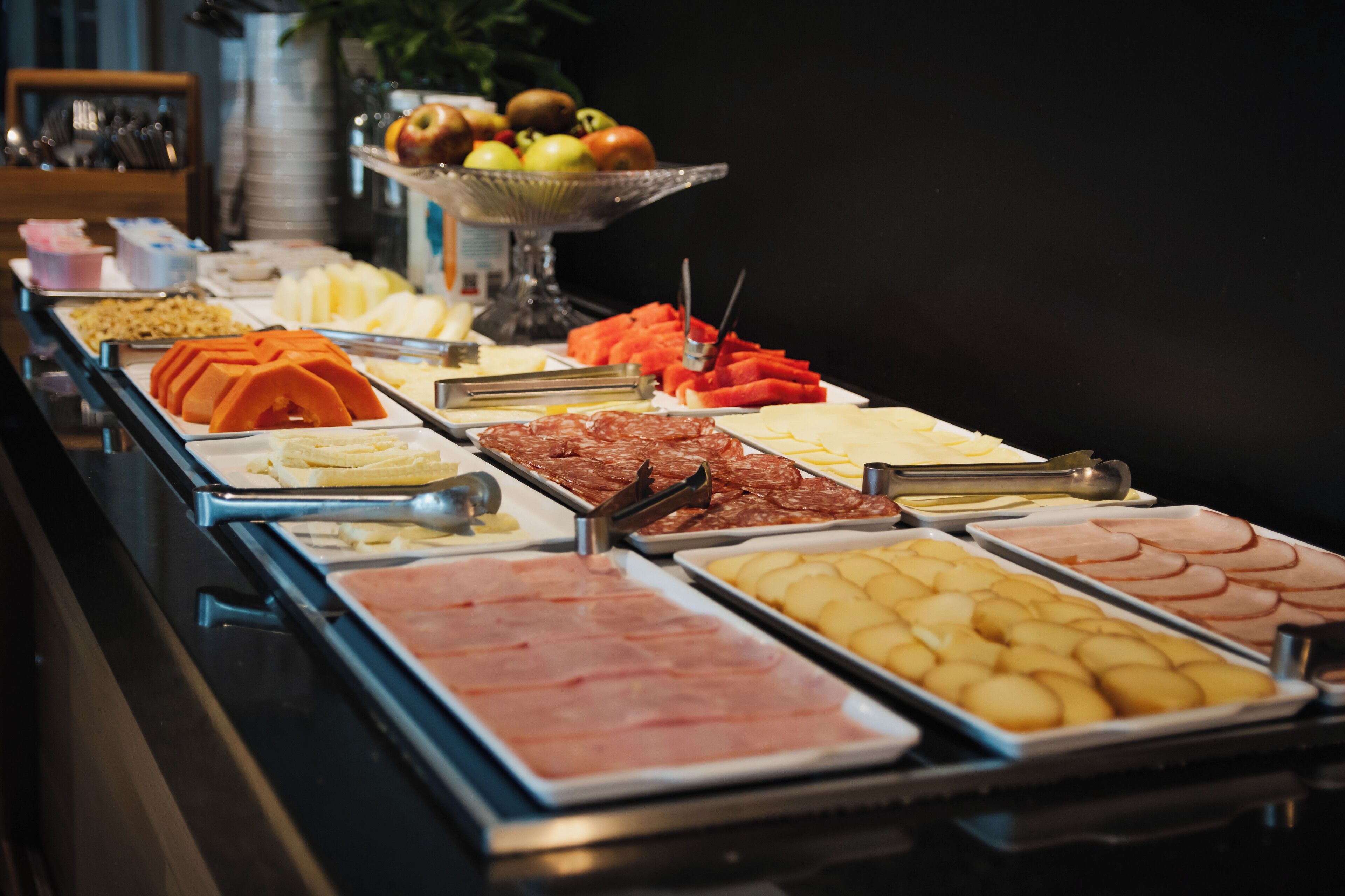 A buffet with various food items including meats, cheeses, and fruits.