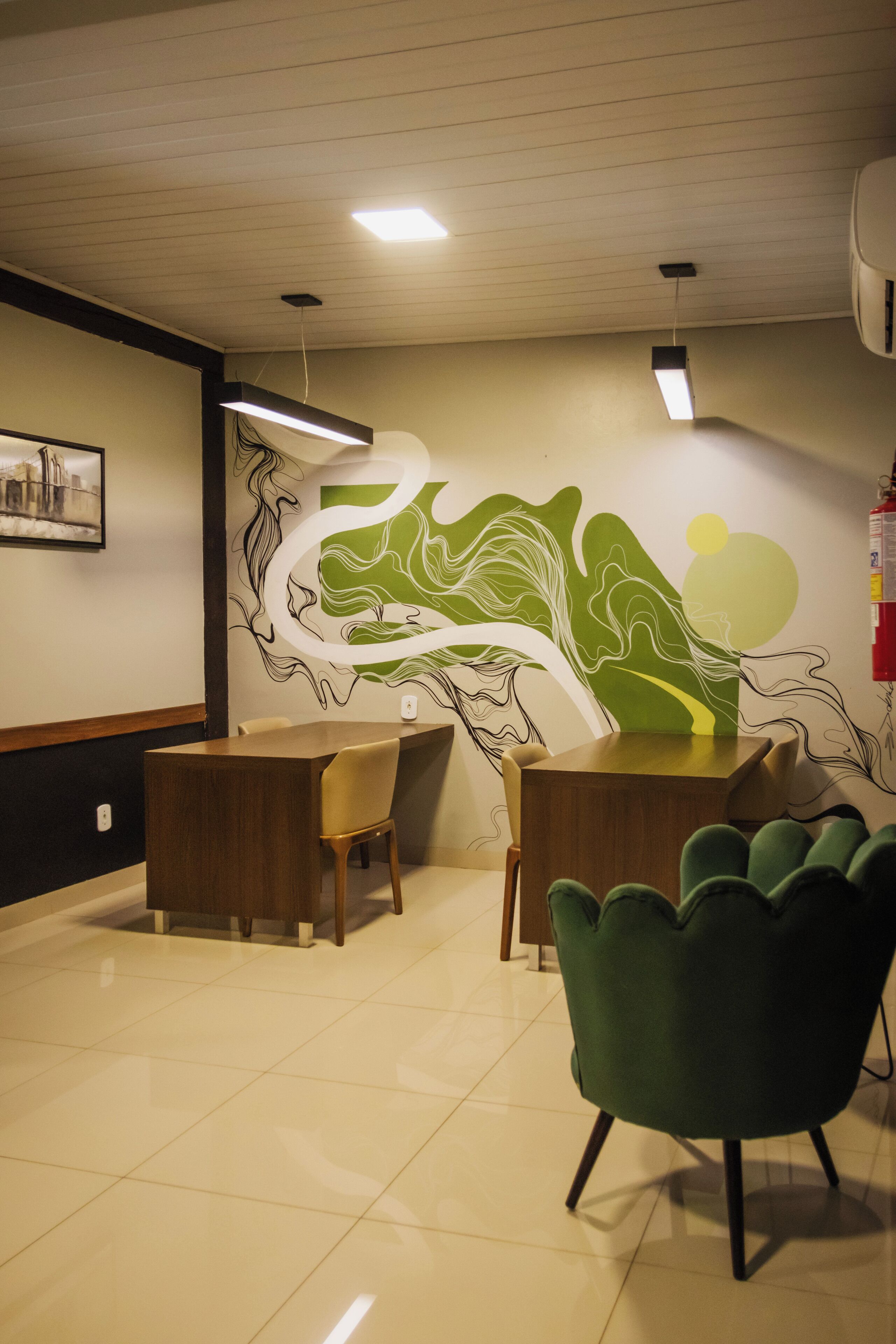 A modern interior with a wooden reception desk, two chairs, a green armchair, and a wall mural.