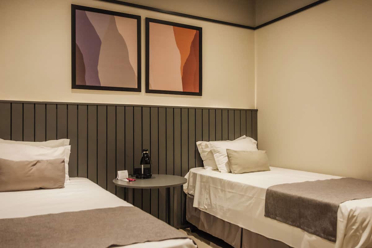 Habitación de hotel con dos camas, una mesita redonda con cafetera y arte abstracto en la pared.