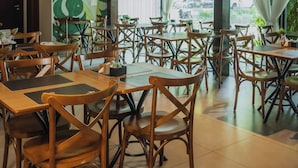 A restaurant with wooden tables and chairs, a chandelier, and a mural of green leaves on the wall. - Hotel Avenida (Sorriso)