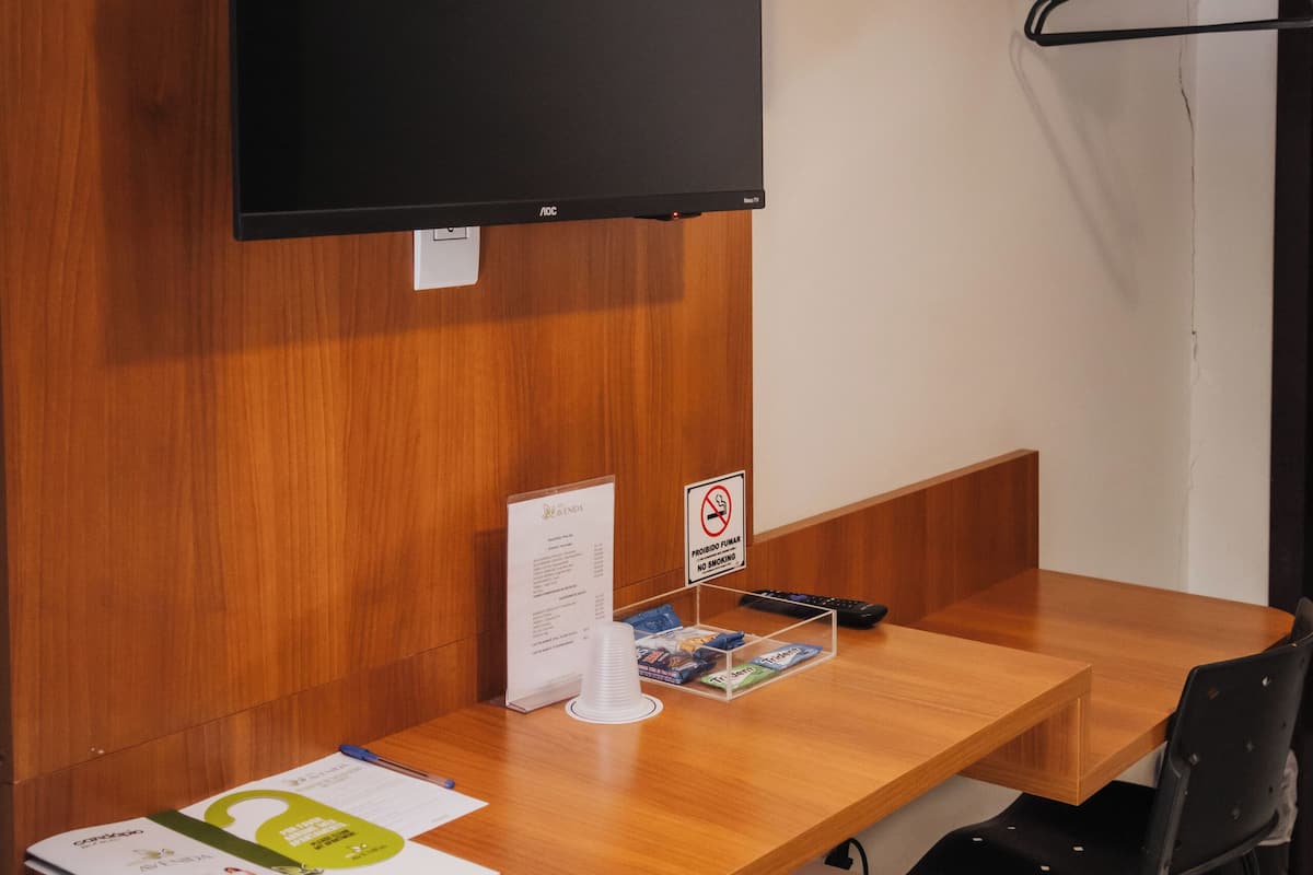 Una habitación de hotel compacta con escritorio de madera, televisor de pantalla plana, refrigerador pequeño y perchero.